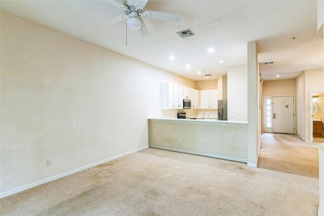 unfurnished living room featuring light carpet, sink, and ceiling fan