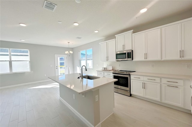 kitchen with appliances with stainless steel finishes, a kitchen island with sink, sink, decorative light fixtures, and white cabinetry