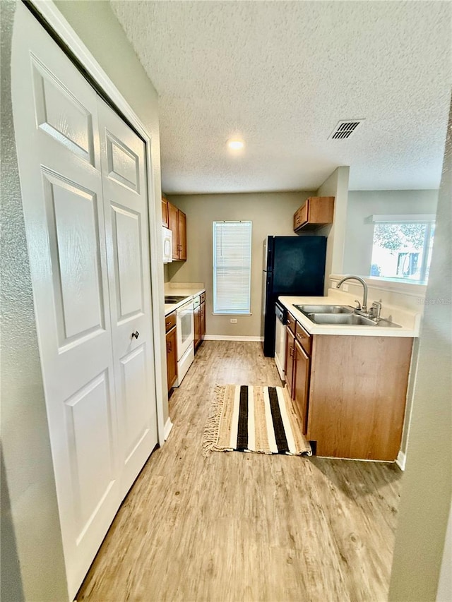 kitchen featuring white appliances, a textured ceiling, sink, and light wood-type flooring