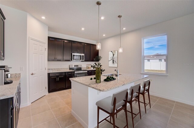 kitchen with appliances with stainless steel finishes, a kitchen breakfast bar, light stone counters, dark brown cabinets, and decorative light fixtures