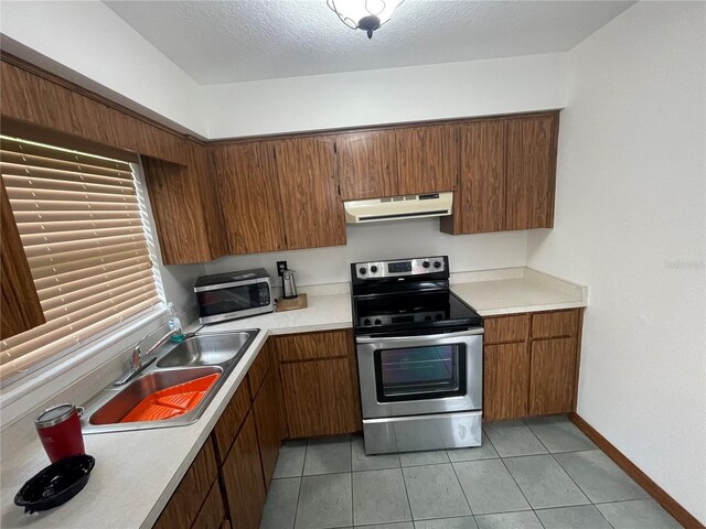 kitchen with a textured ceiling, light tile patterned flooring, sink, range hood, and stainless steel appliances