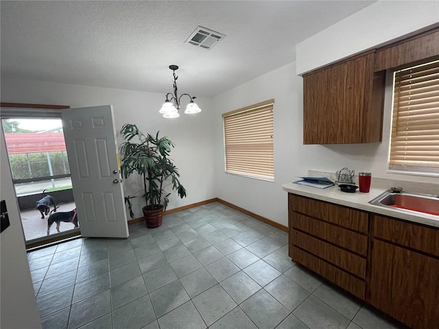 kitchen featuring hanging light fixtures, light tile patterned floors, sink, a textured ceiling, and a notable chandelier