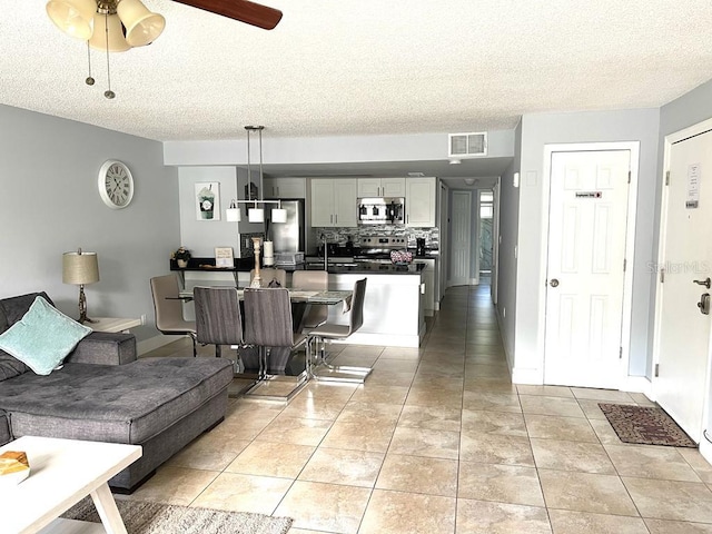 living room with ceiling fan, light tile patterned floors, and a textured ceiling