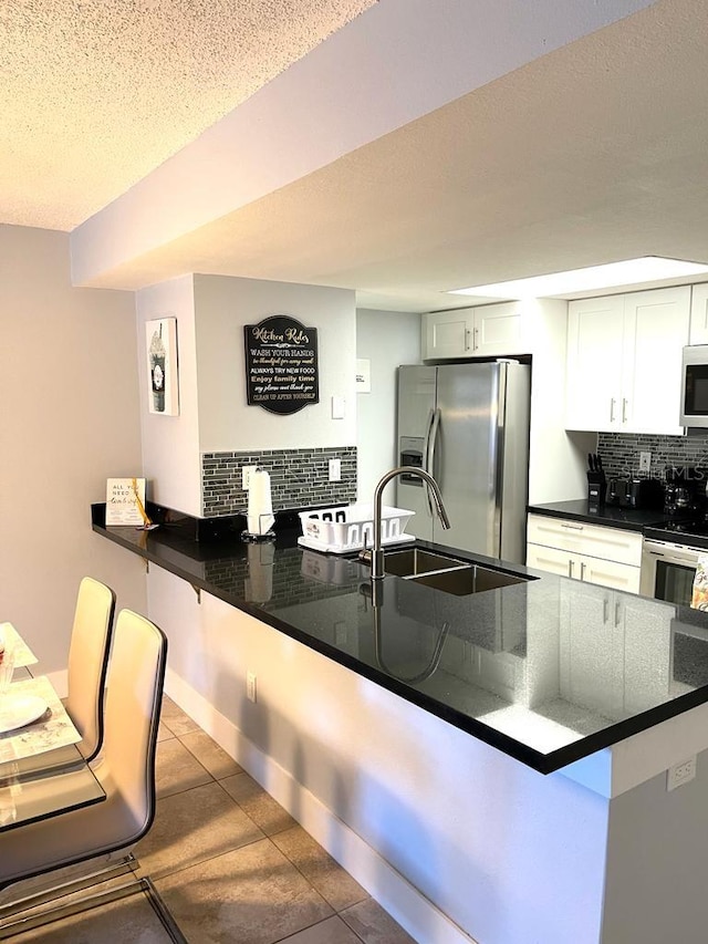 kitchen with kitchen peninsula, decorative backsplash, stainless steel appliances, and white cabinetry