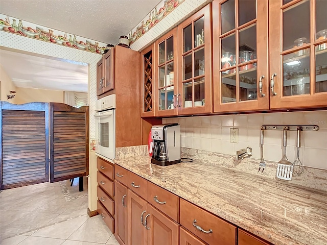 kitchen with light stone countertops, tasteful backsplash, a textured ceiling, white oven, and light tile patterned flooring