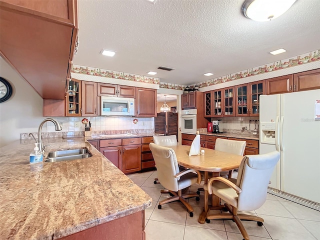 kitchen with light stone countertops, sink, white appliances, decorative backsplash, and light tile patterned floors