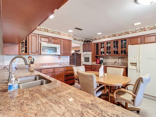 kitchen with light stone countertops, tasteful backsplash, a textured ceiling, white appliances, and sink