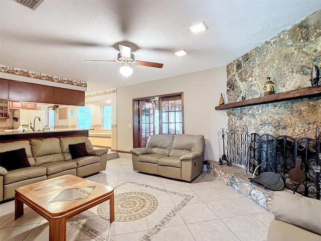 tiled living room featuring ceiling fan, a fireplace, and a textured ceiling