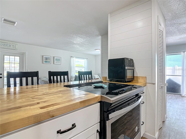 kitchen with light wood-type flooring, a textured ceiling, stainless steel electric stove, and a healthy amount of sunlight