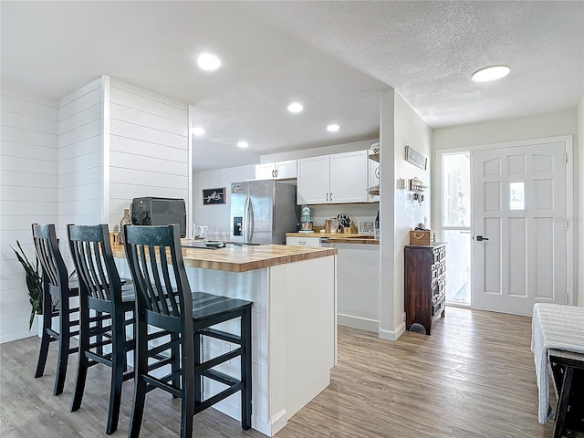 kitchen featuring white cabinetry, a breakfast bar area, wooden counters, light wood-type flooring, and stainless steel refrigerator with ice dispenser