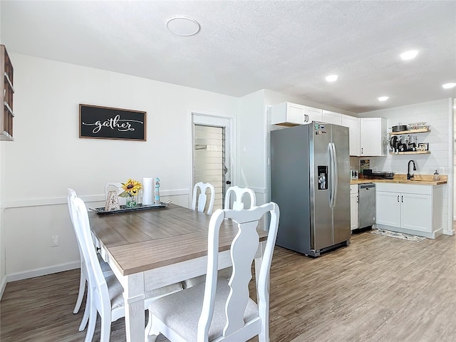 dining area with a textured ceiling, sink, and light hardwood / wood-style floors