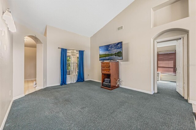 unfurnished living room with high vaulted ceiling and dark colored carpet