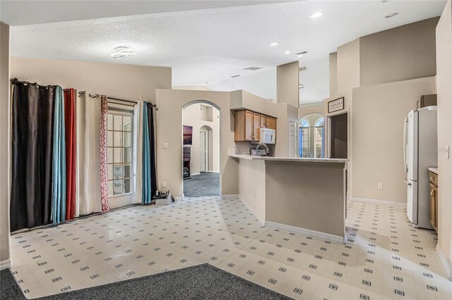 kitchen with fridge, light colored carpet, a textured ceiling, and high vaulted ceiling