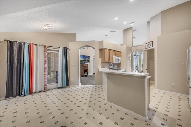 kitchen featuring light brown cabinets, kitchen peninsula, a textured ceiling, stainless steel range, and vaulted ceiling