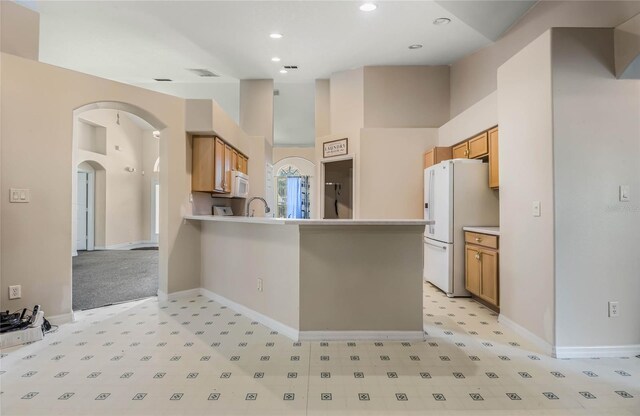 kitchen featuring sink, kitchen peninsula, white appliances, a high ceiling, and light colored carpet