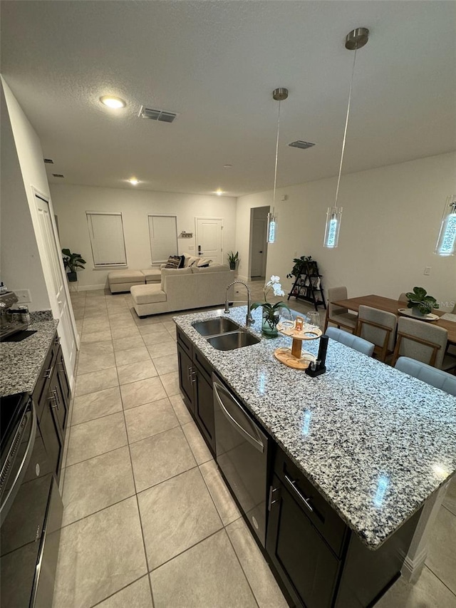 kitchen featuring light stone counters, pendant lighting, stainless steel dishwasher, a kitchen island with sink, and sink