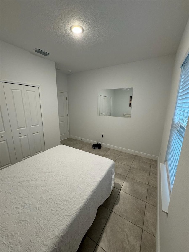 bedroom with a textured ceiling, tile patterned floors, and a closet