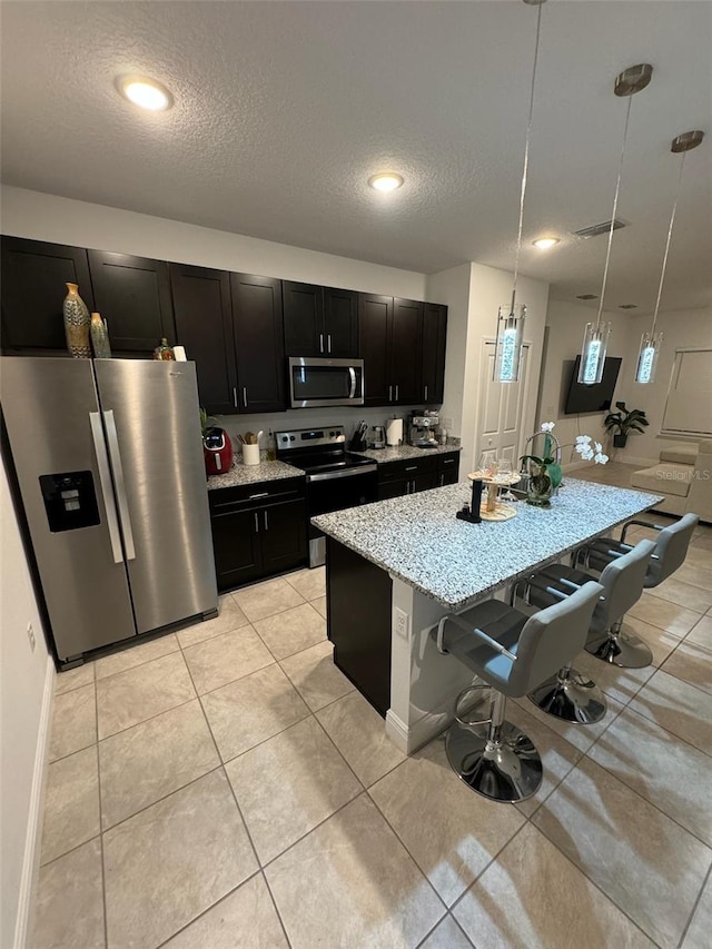 kitchen featuring decorative light fixtures, a textured ceiling, appliances with stainless steel finishes, and a kitchen breakfast bar