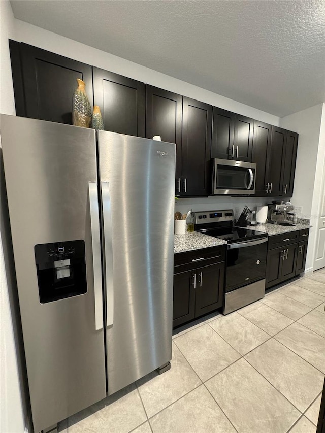 kitchen with light stone countertops, a textured ceiling, appliances with stainless steel finishes, and light tile patterned floors