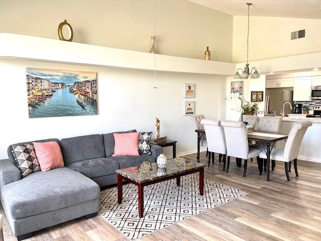 living room featuring a textured ceiling, light hardwood / wood-style flooring, an inviting chandelier, and high vaulted ceiling