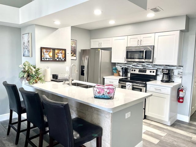 kitchen with sink, stainless steel appliances, kitchen peninsula, a kitchen bar, and white cabinets