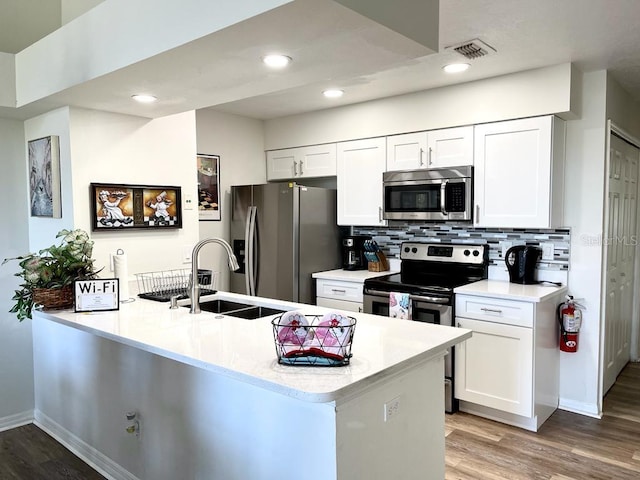 kitchen with white cabinetry, sink, stainless steel appliances, kitchen peninsula, and light wood-type flooring