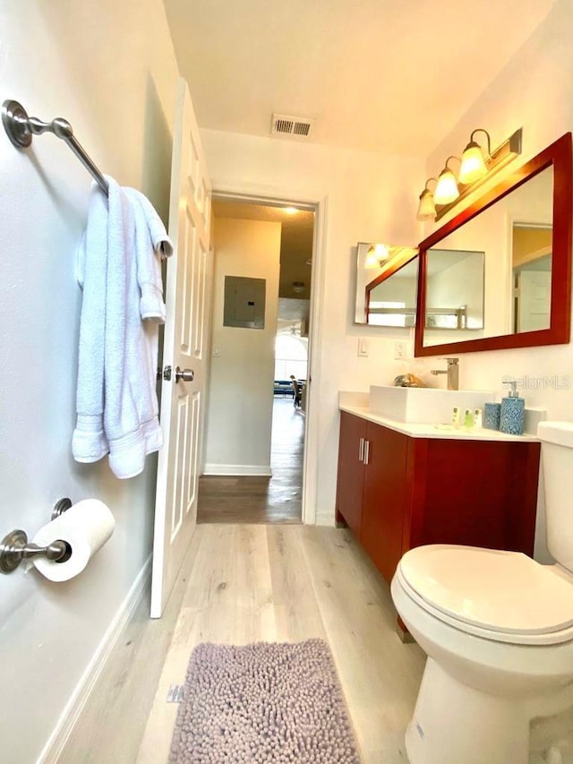 bathroom featuring hardwood / wood-style floors, vanity, electric panel, and toilet