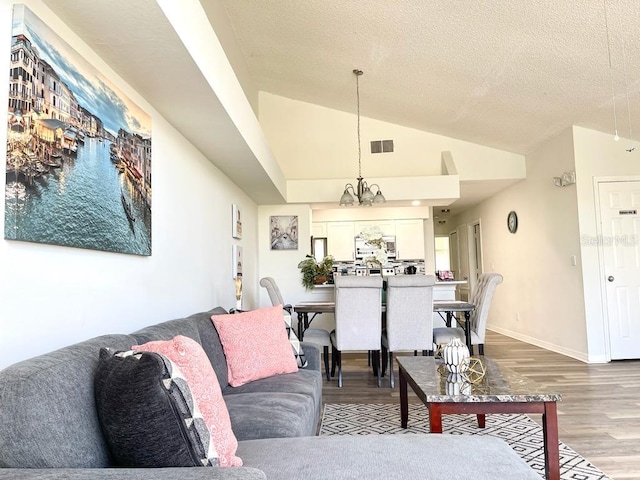 living room featuring a textured ceiling, wood-type flooring, vaulted ceiling, and an inviting chandelier