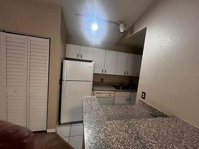 kitchen with white cabinets, white appliances, light tile patterned floors, dark stone counters, and sink