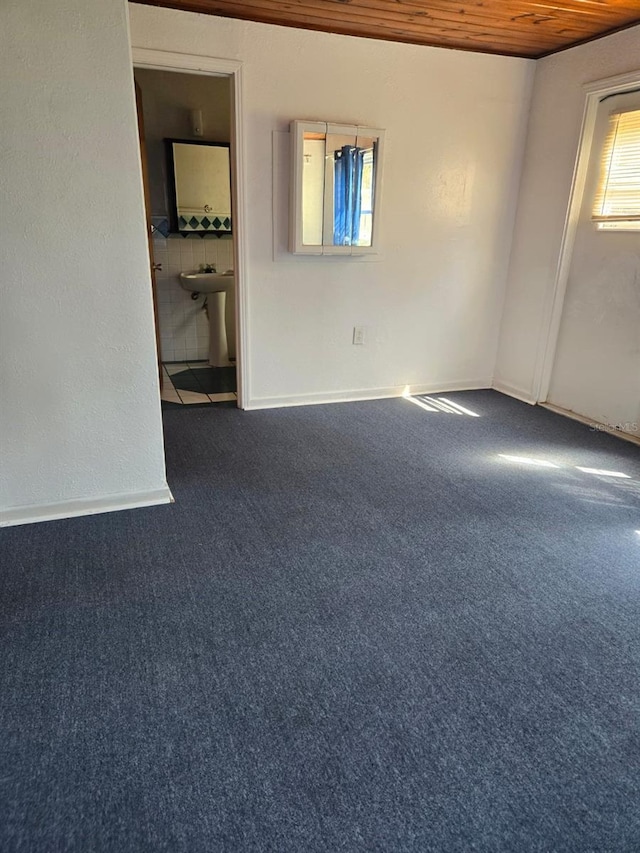 spare room featuring wood ceiling and dark colored carpet