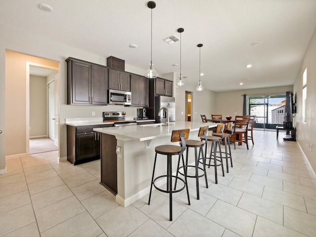 kitchen featuring dark brown cabinets, a breakfast bar, an island with sink, hanging light fixtures, and appliances with stainless steel finishes