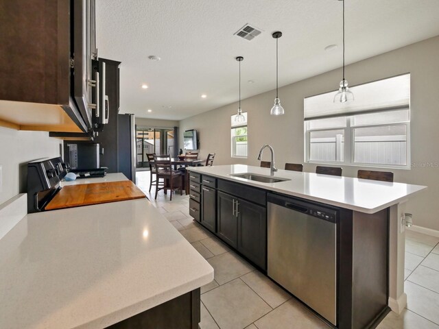 kitchen with dark brown cabinetry, pendant lighting, sink, stainless steel dishwasher, and a kitchen island with sink