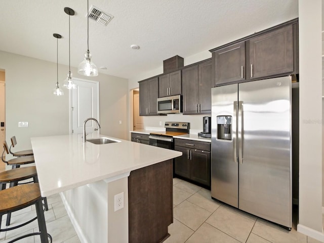 kitchen with sink, dark brown cabinets, decorative light fixtures, a kitchen island with sink, and appliances with stainless steel finishes