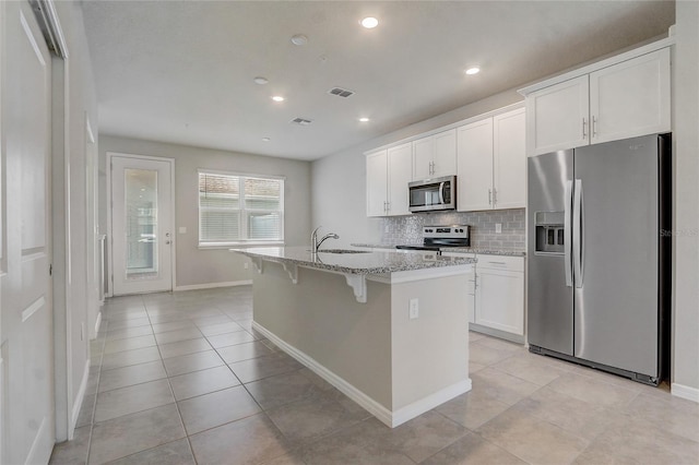 kitchen featuring sink, white cabinets, stainless steel appliances, a center island with sink, and light stone countertops