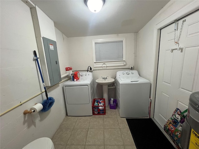 laundry area with light tile patterned floors, sink, electric panel, and washing machine and clothes dryer