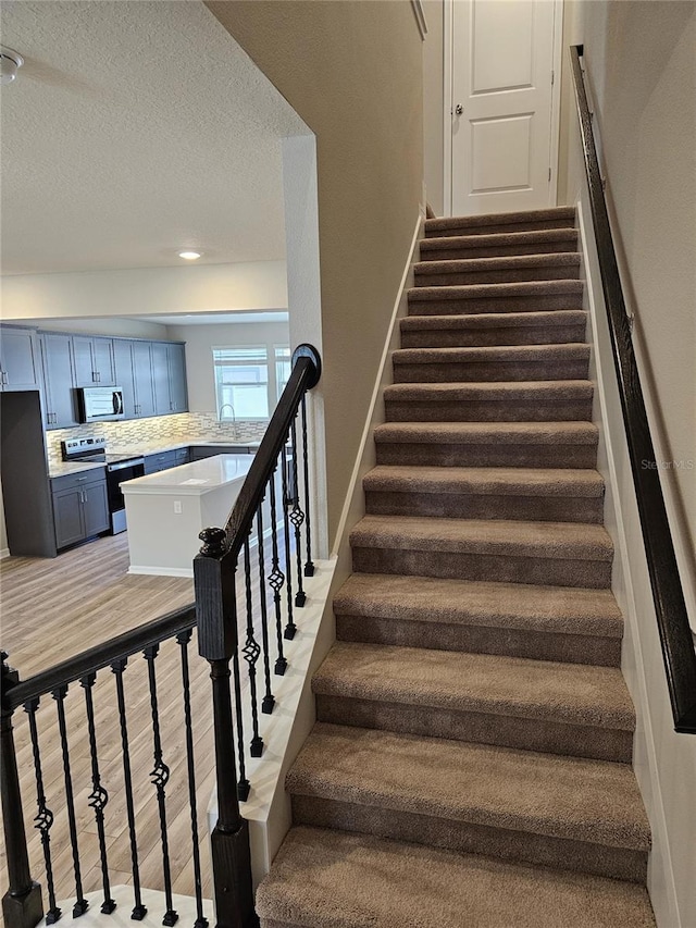 stairway with a textured ceiling, sink, and hardwood / wood-style flooring