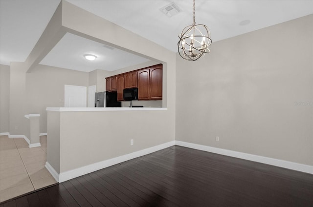 kitchen featuring light wood-type flooring, black appliances, kitchen peninsula, and hanging light fixtures