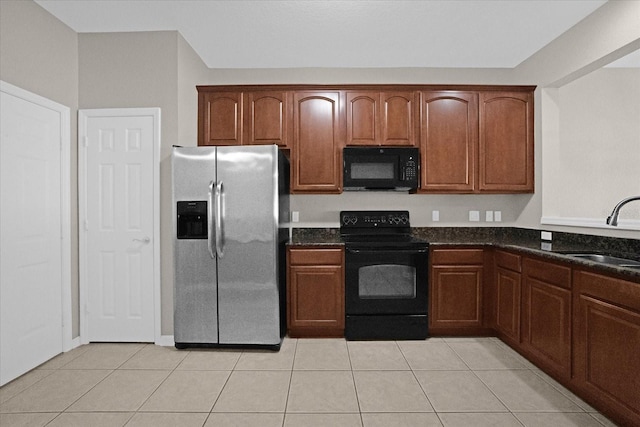 kitchen with dark stone countertops, light tile patterned floors, sink, and black appliances