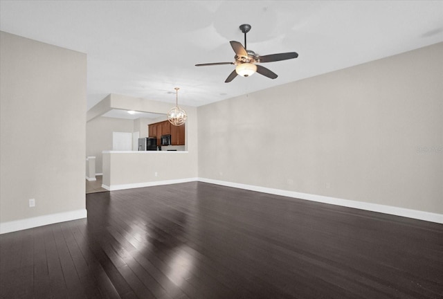 unfurnished living room with ceiling fan with notable chandelier and dark hardwood / wood-style floors