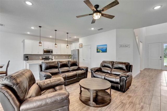 living room featuring light wood-type flooring, a textured ceiling, and ceiling fan