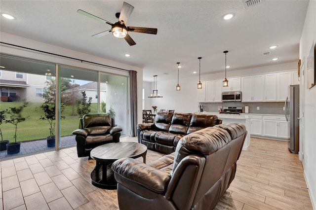 living room with ceiling fan, a textured ceiling, and light hardwood / wood-style floors