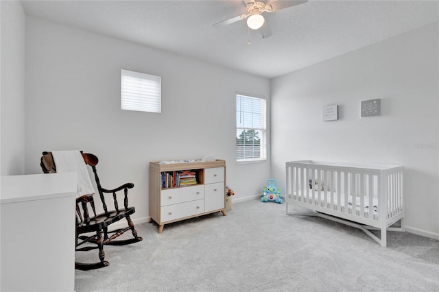 bedroom featuring light carpet, ceiling fan, and a crib