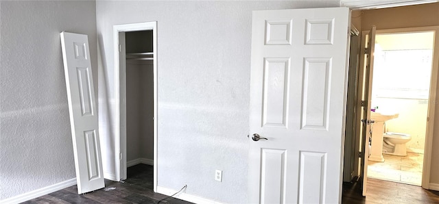 bedroom with connected bathroom, dark wood-type flooring, and a closet