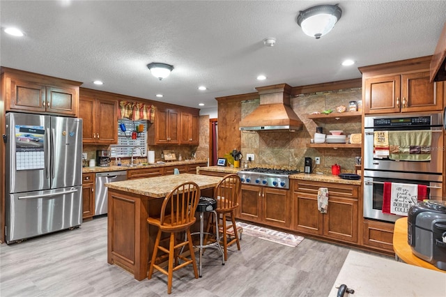 kitchen featuring a kitchen island, appliances with stainless steel finishes, custom range hood, and light hardwood / wood-style floors