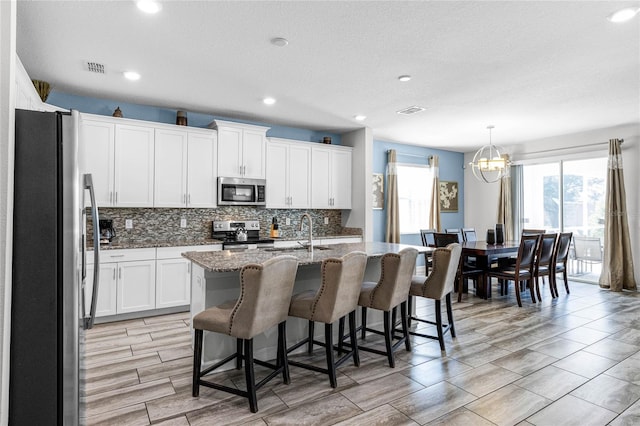 kitchen featuring a breakfast bar area, white cabinets, an island with sink, and stainless steel appliances