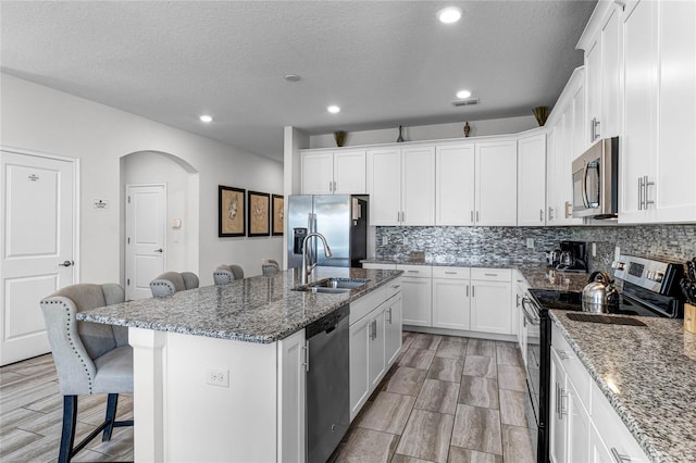 kitchen featuring a kitchen bar, appliances with stainless steel finishes, a kitchen island with sink, stone countertops, and sink