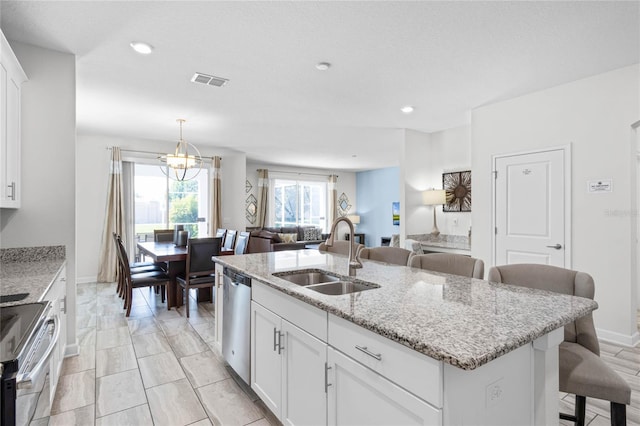 kitchen featuring a kitchen bar, white cabinetry, sink, light stone counters, and a center island with sink