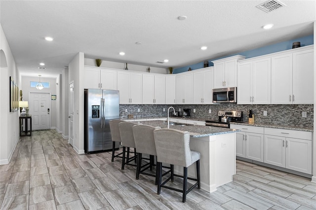 kitchen with appliances with stainless steel finishes, sink, white cabinetry, and a kitchen island with sink