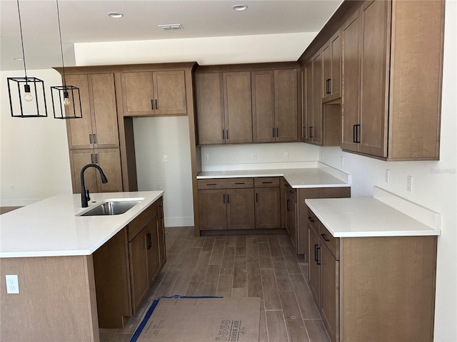 kitchen with decorative light fixtures, sink, and an island with sink