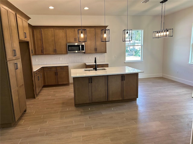 kitchen with tasteful backsplash, sink, a center island with sink, and decorative light fixtures